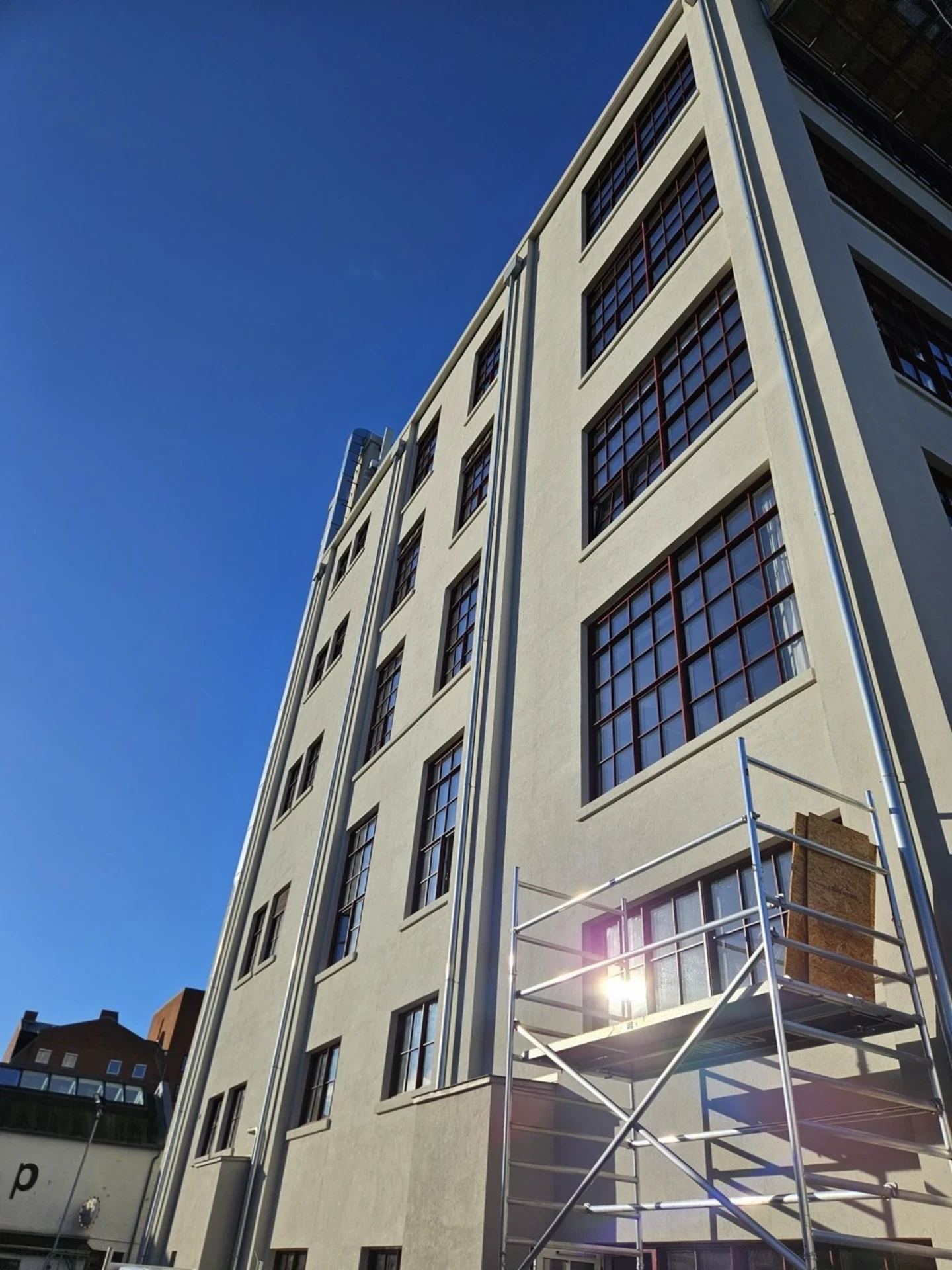 Moderne kontorbygning med store vinduer og klar himmel, under opførelse.