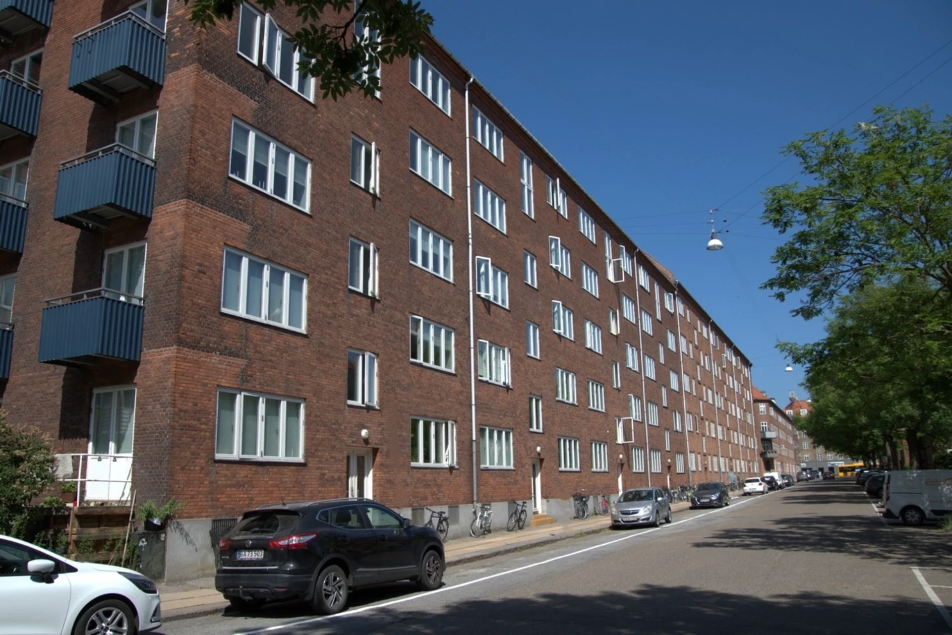 Boligbygning i København med flere etager og parkeringsplads foran.