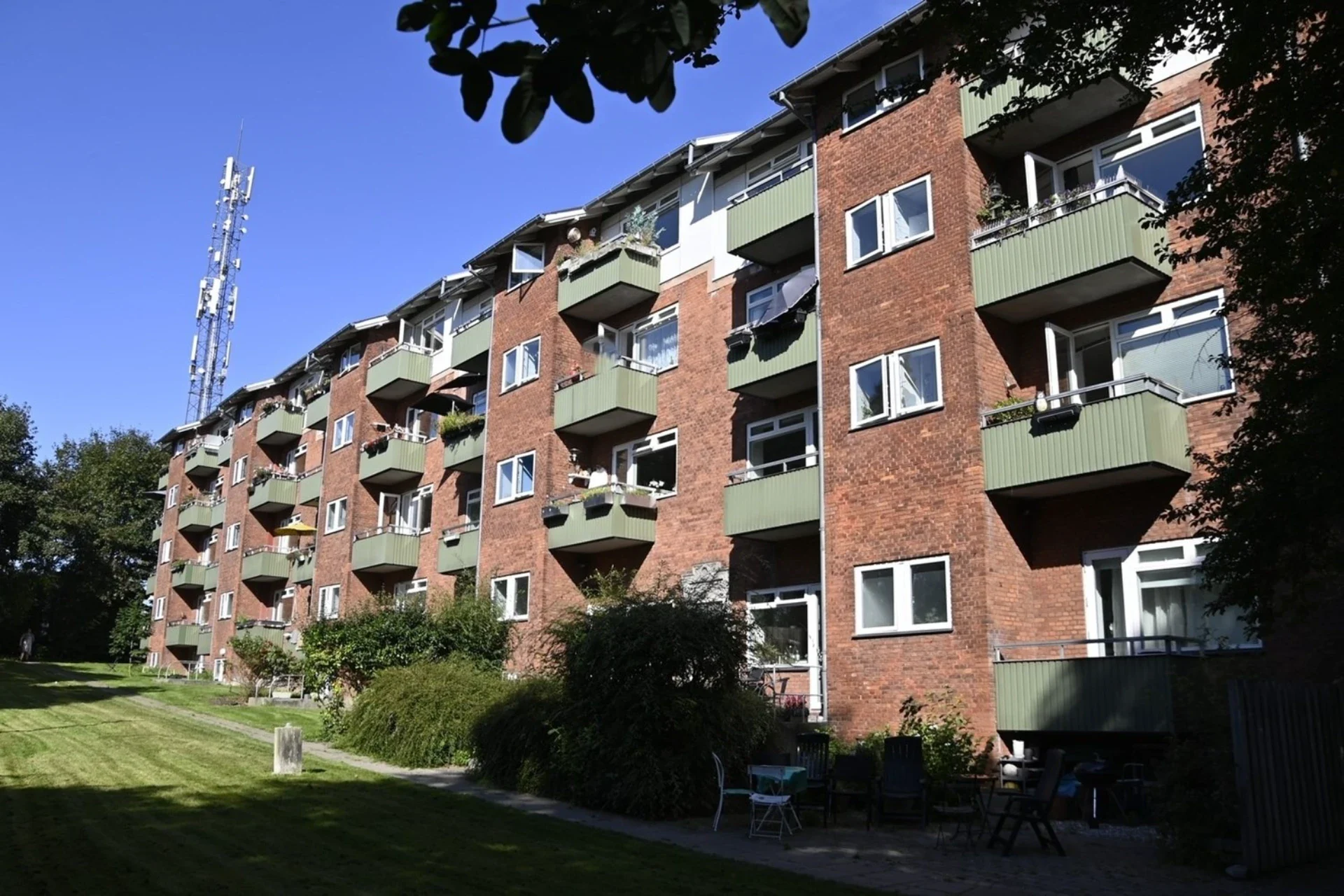 Flot boligbygning med grønne balkoner og velholdt have.