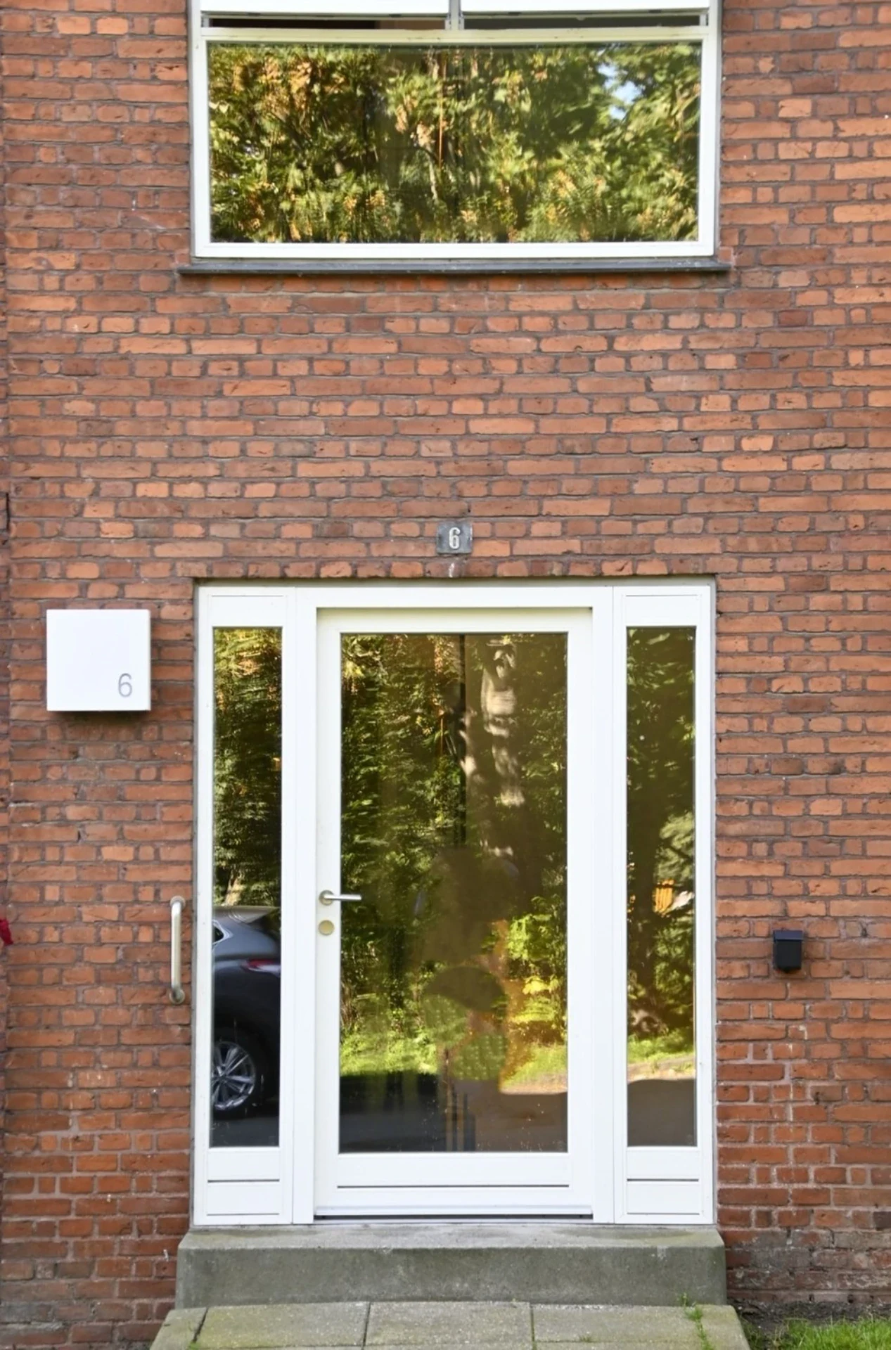 Glasindgang med reflekterende vindue og dør foran en murstensbygning.