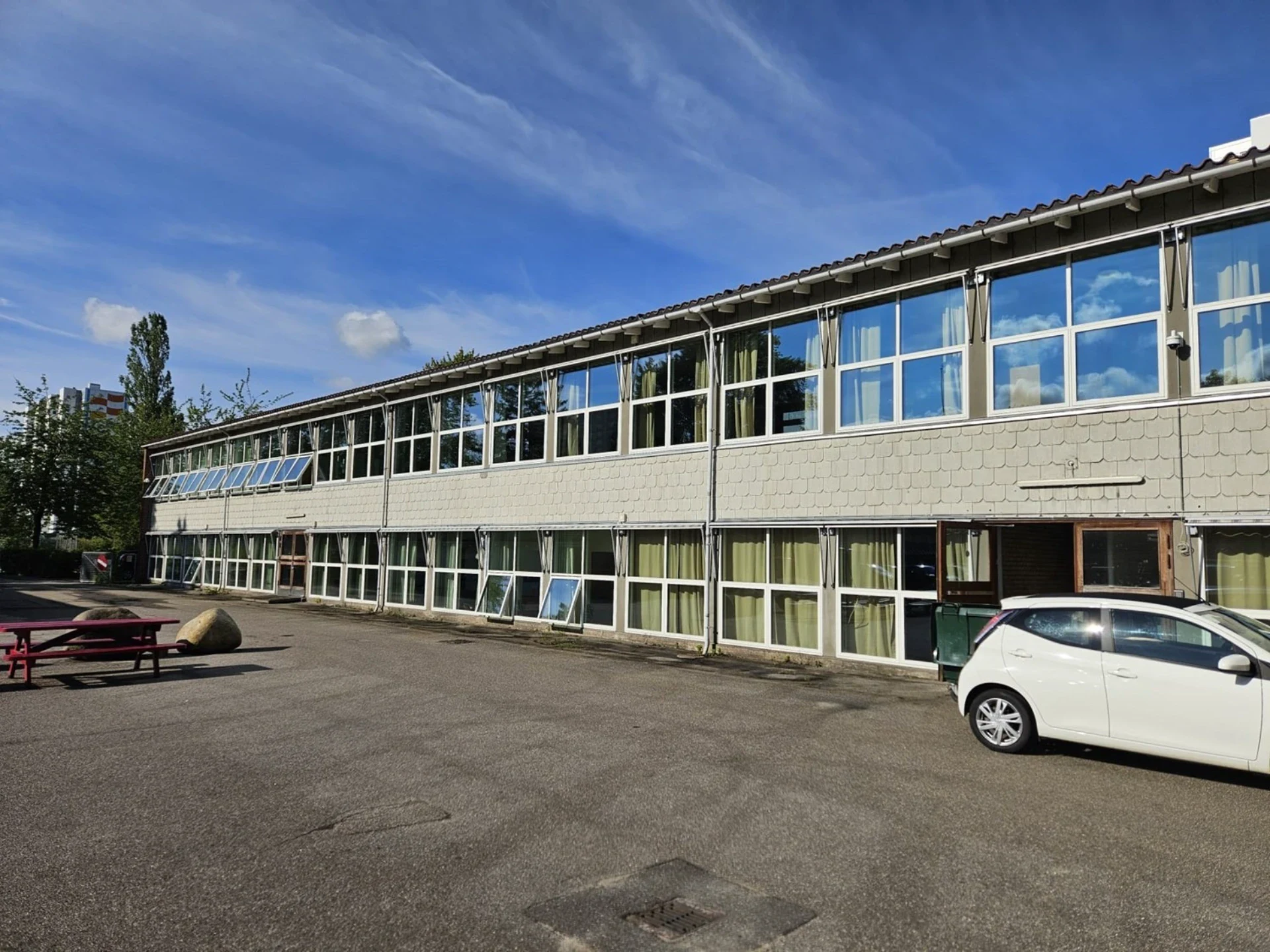 Kontorbygning med store vinduer og parkeringsplads.
