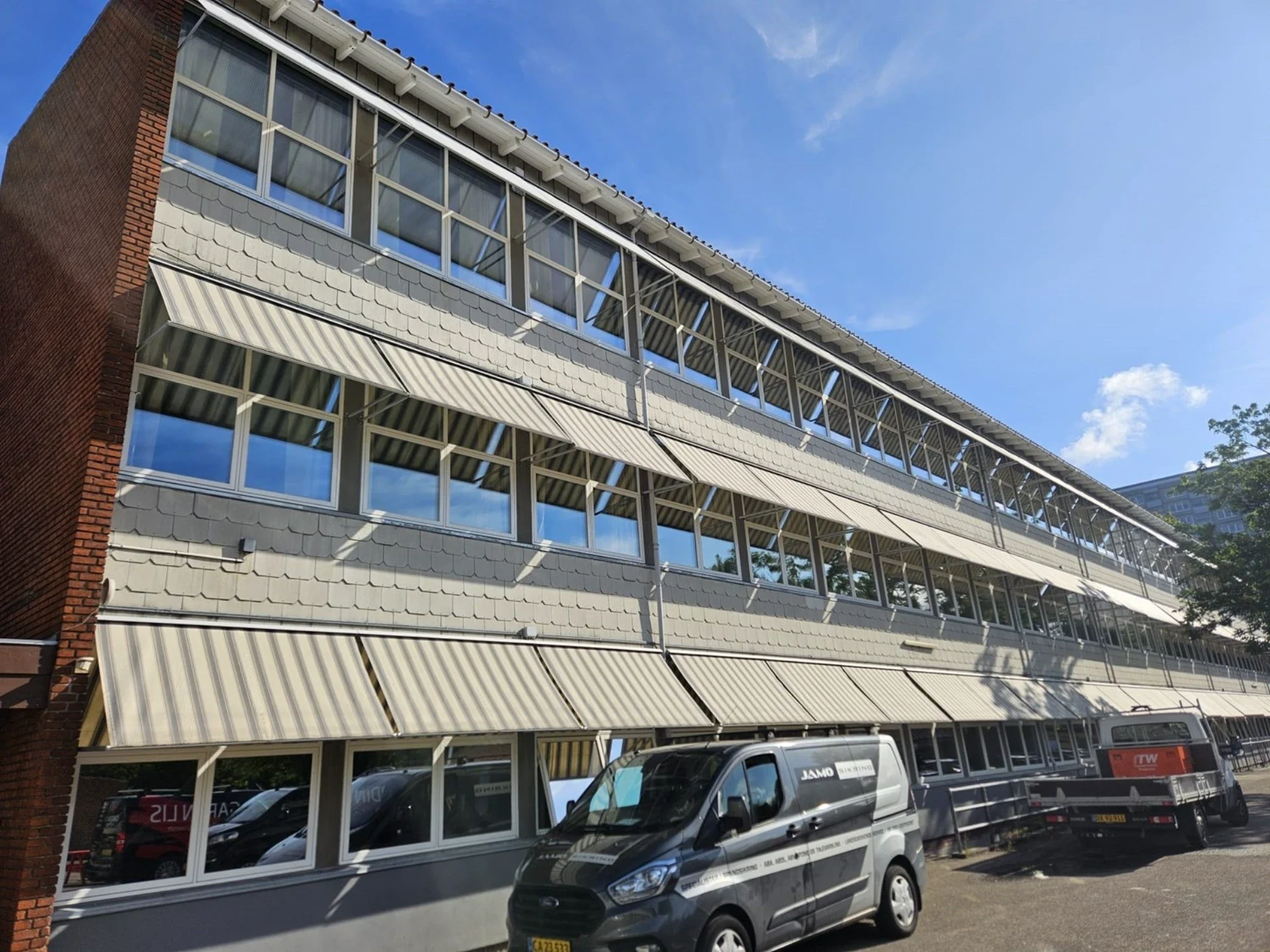 Høj kontorbygning med store vinduespartier og markiseudskæringer.