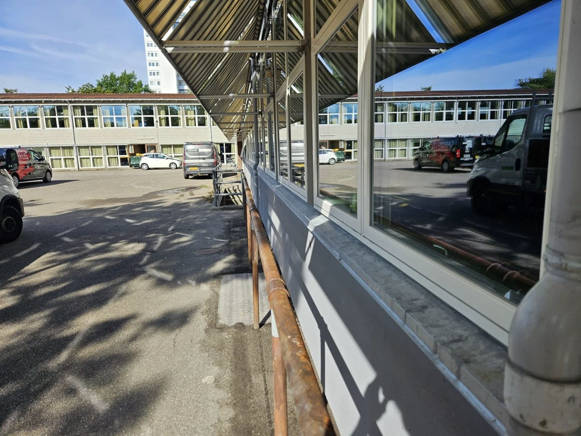Kontorbygning med store vinduer og parkeringsplads i baggrunden.