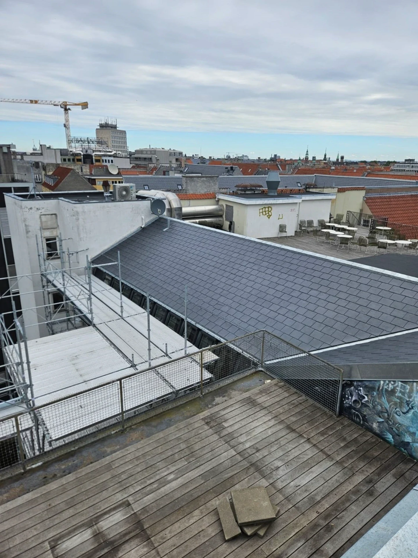 Tag på en bybygning med tagrender og tagpap under en overskyet himmel.