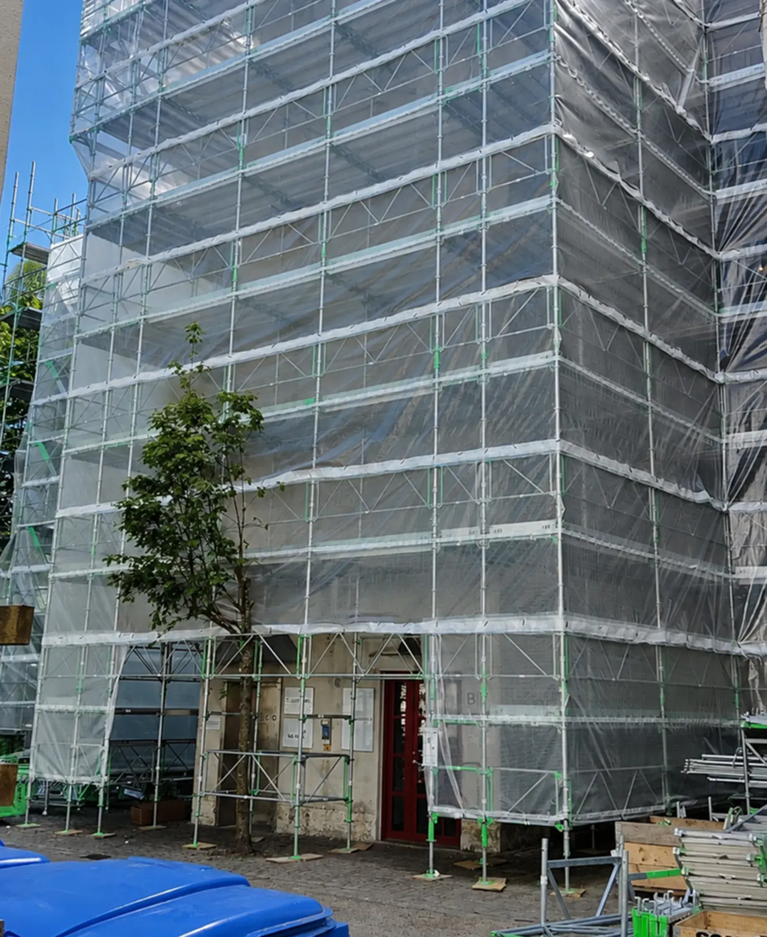 Bygningsfacade under stilladsopsætning med beskyttelsesnet og scaffolding.